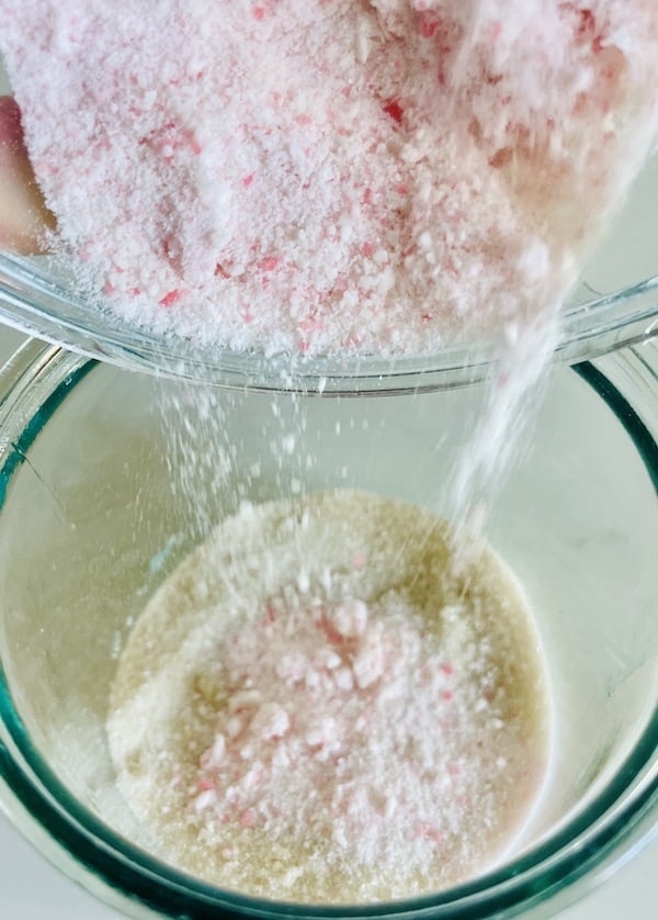 Crushed candy canes being poured into a cup of sugar.