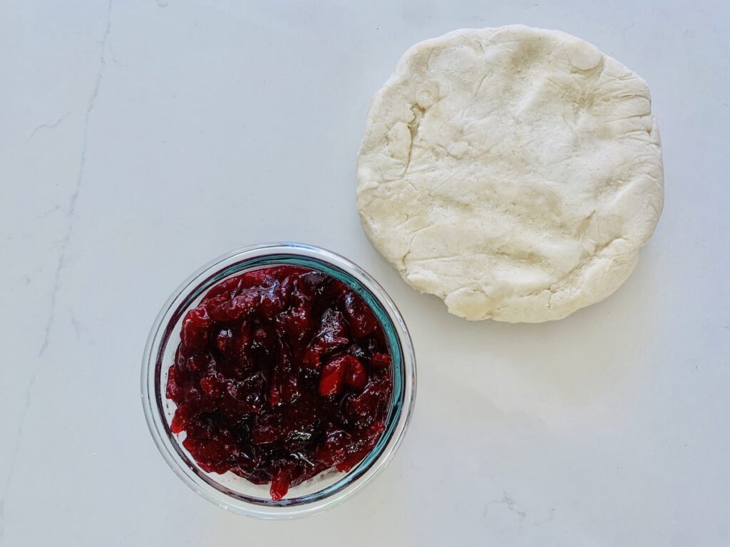 Birds eye view: pie dough disk and bowl of cranberry sauce.