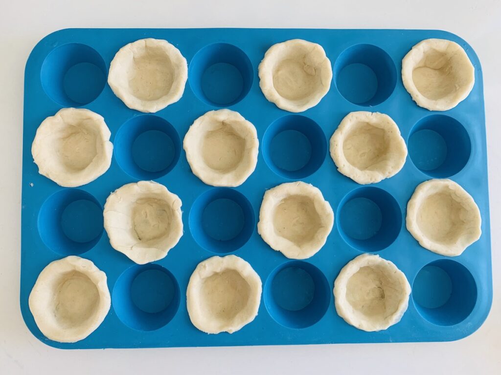 Birds eye view: blue mini silicone muffin pan with 12 of the spots filled with pie crust and 12 empty.