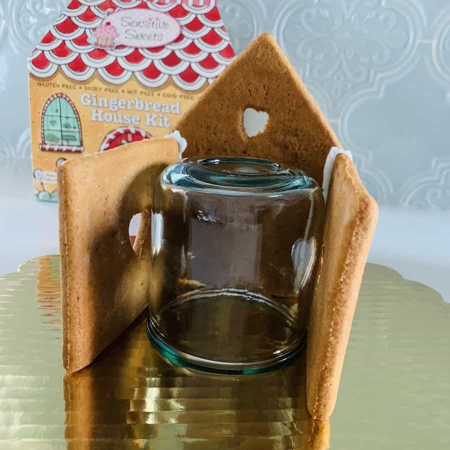 A glass jar supporting 3 walls of a gluten-free gingerbread house while being glued together.