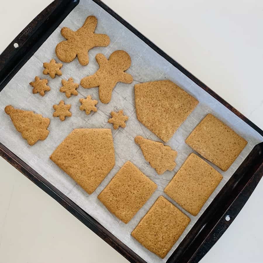 A baking sheet with baked gluten-free gingerbread house pieces, trees, men, and snowflakes.