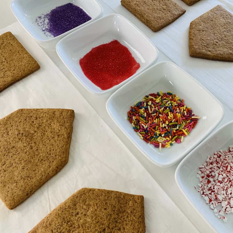 Unassembled pieces of a gluten-free gingerbread house with small bowls of sprinkles.