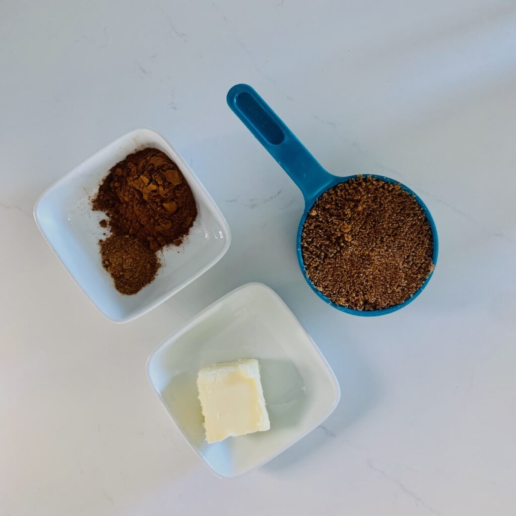 Birds Eye view: blue measuring cup with brown sugar, square white bowls with butter and brown spices.