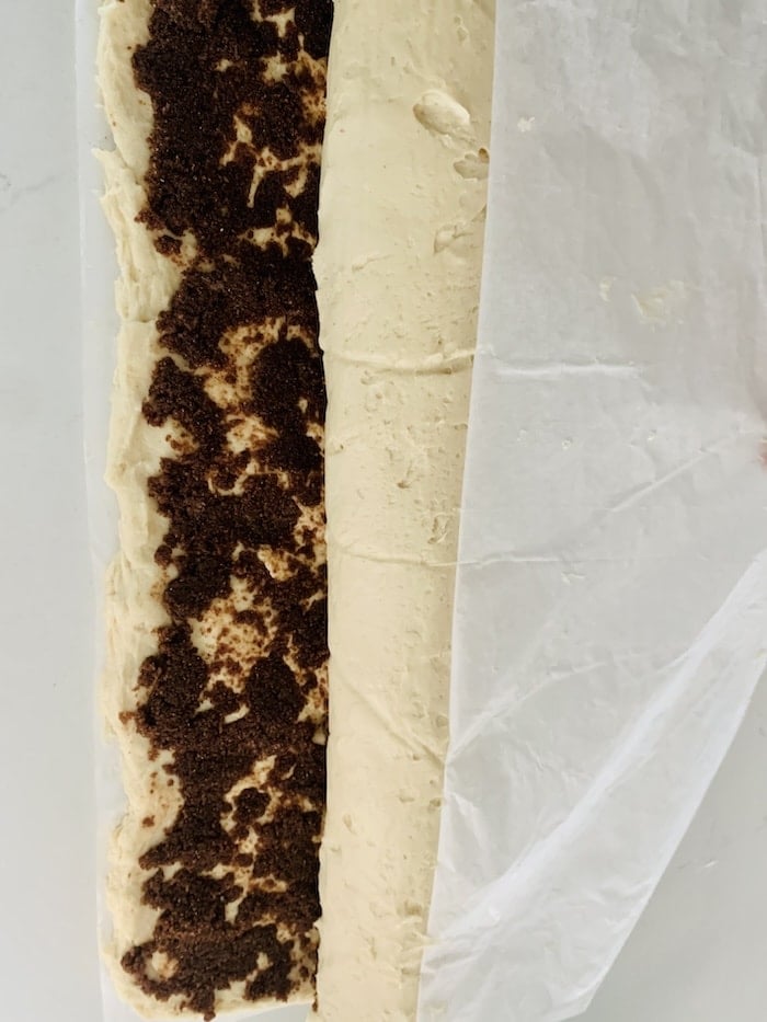 Birds Eye view: The dough rectangle almost fully rolled into a log with just a couple of inches of cinnamon-filling-covered dough still needing to be rolled, and more parchment paper being pulled back from the roll.