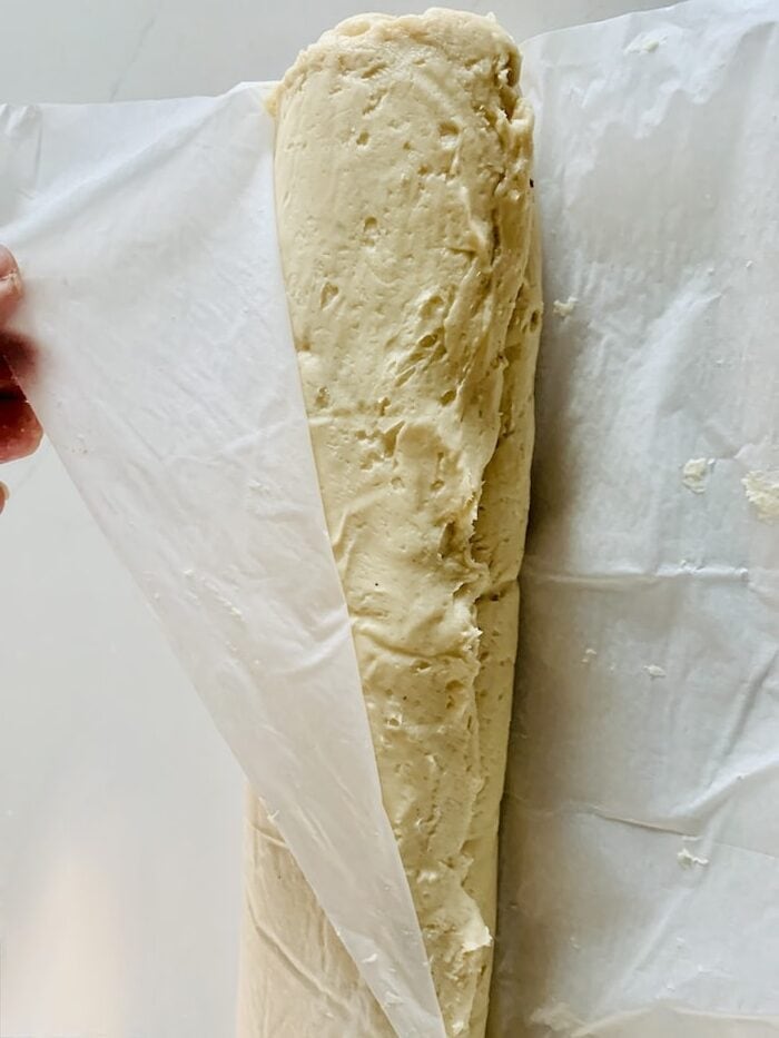 Birds Eye view: the dough completely rolled into a log and the last bit of parchment paper being pulled back to lie flat on the counter under the log.