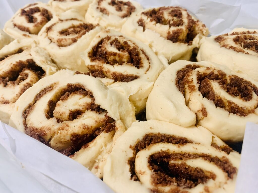 Unbaked, puffed-up, risen cinnamon rolls in a glass baking dish.