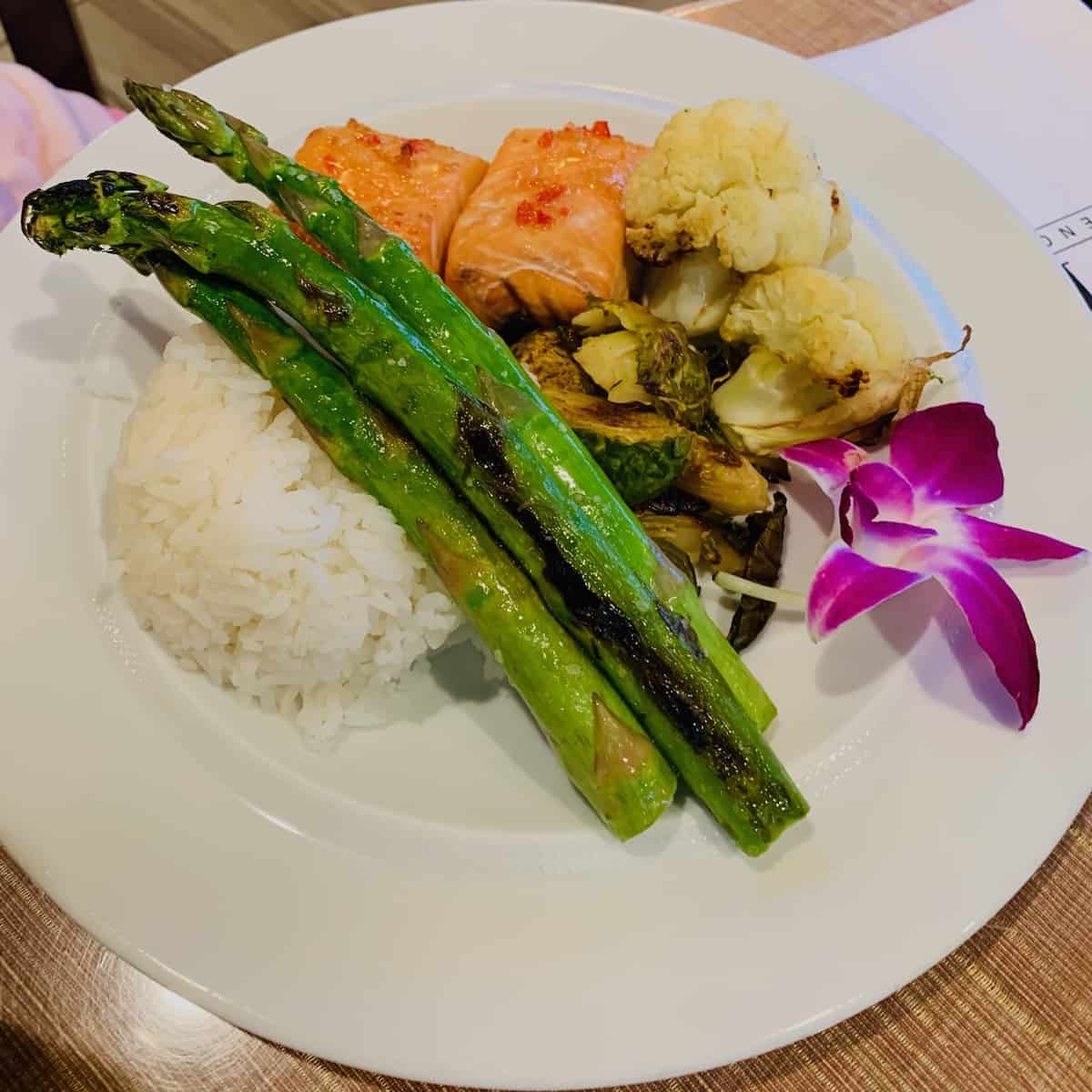 White plate with rice, salmon, asparagus, roasted cauliflower & Brussels spouts and an orchid.
