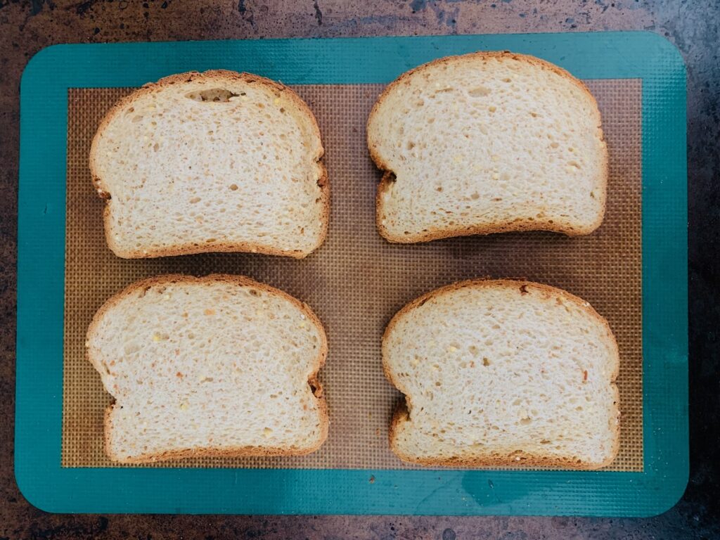 Birds Eye view: four slices of bread on a silicone baking mat on top of a baking sheet.