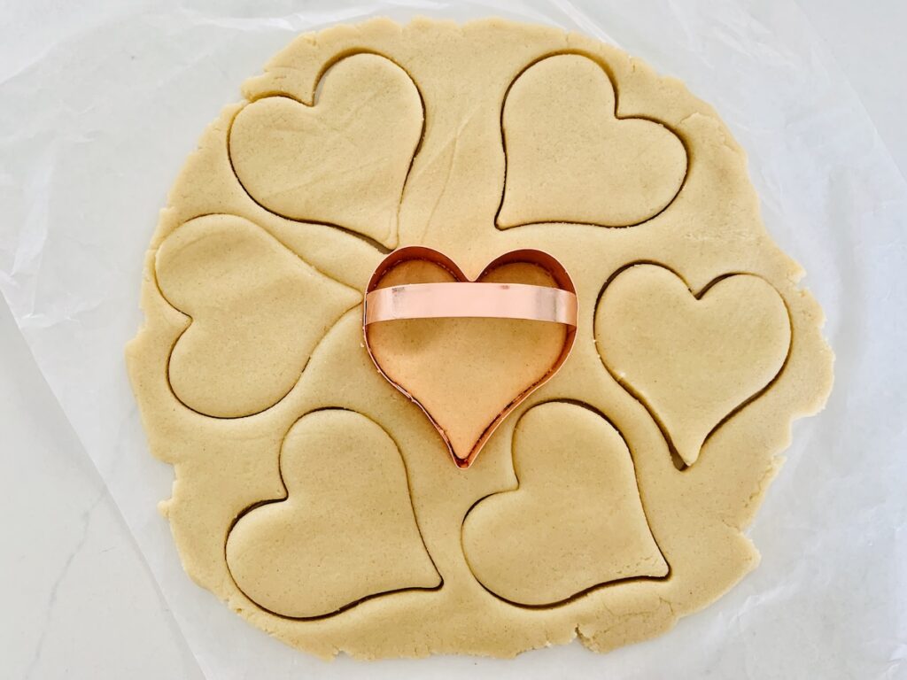 Birds Eye view: rolled out dough with heart shapes cut out and a copper cookie cutter with a handle in the center.