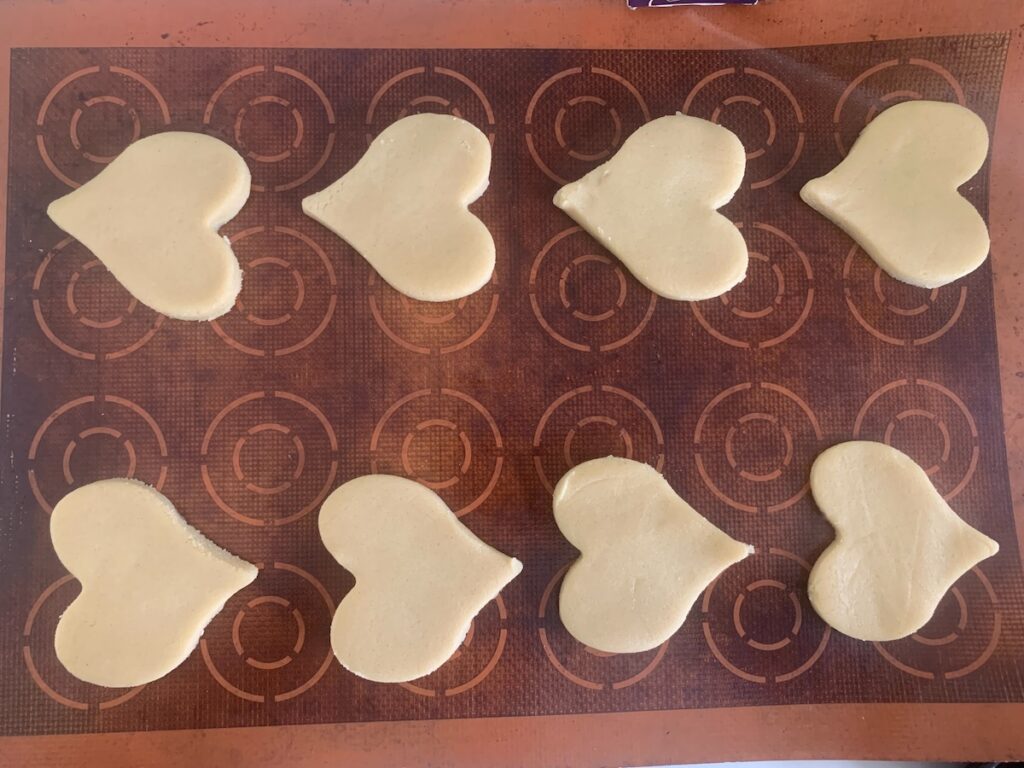 Birds Eye view: 8 unbaked heart cookies in two rows on a silicone baking mat.