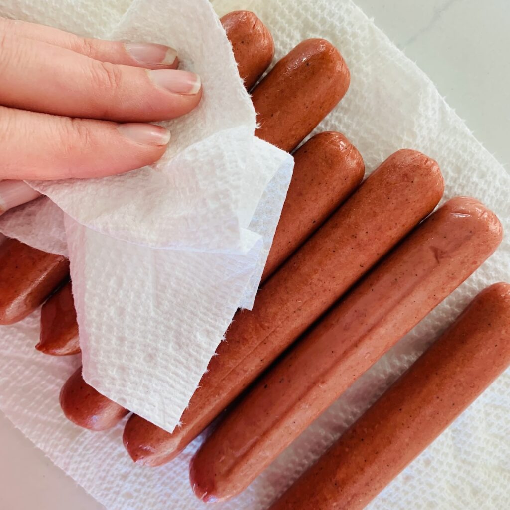 Patting hot dogs with a paper towel.