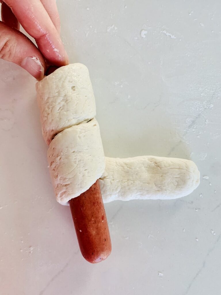 Birds Eye view: wrapping a hot dog with the flattened rope of gluten-free dough.