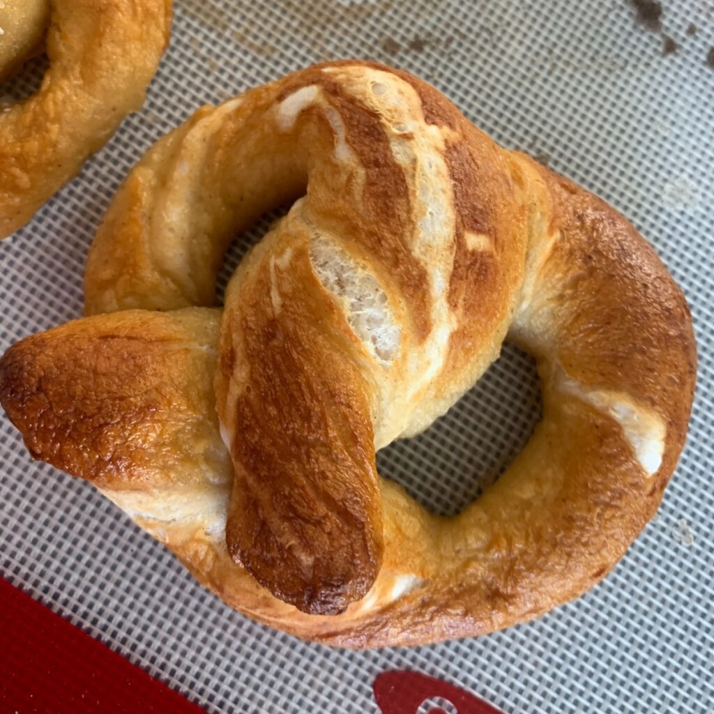 Deep brown soft pretzel on a baking sheet topped with a silicone baking mat.
