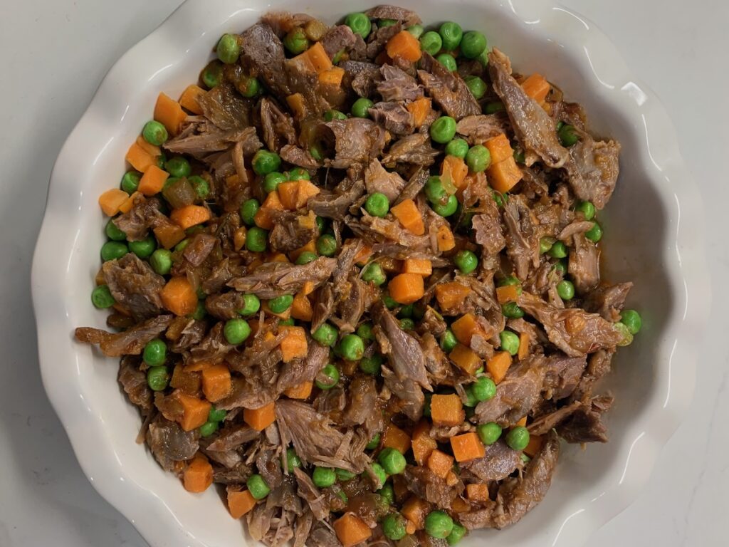 Birds Eye view: shredded lamb, chopped carrots, and peas lightly covered in sauce in a fluted pie dish.
