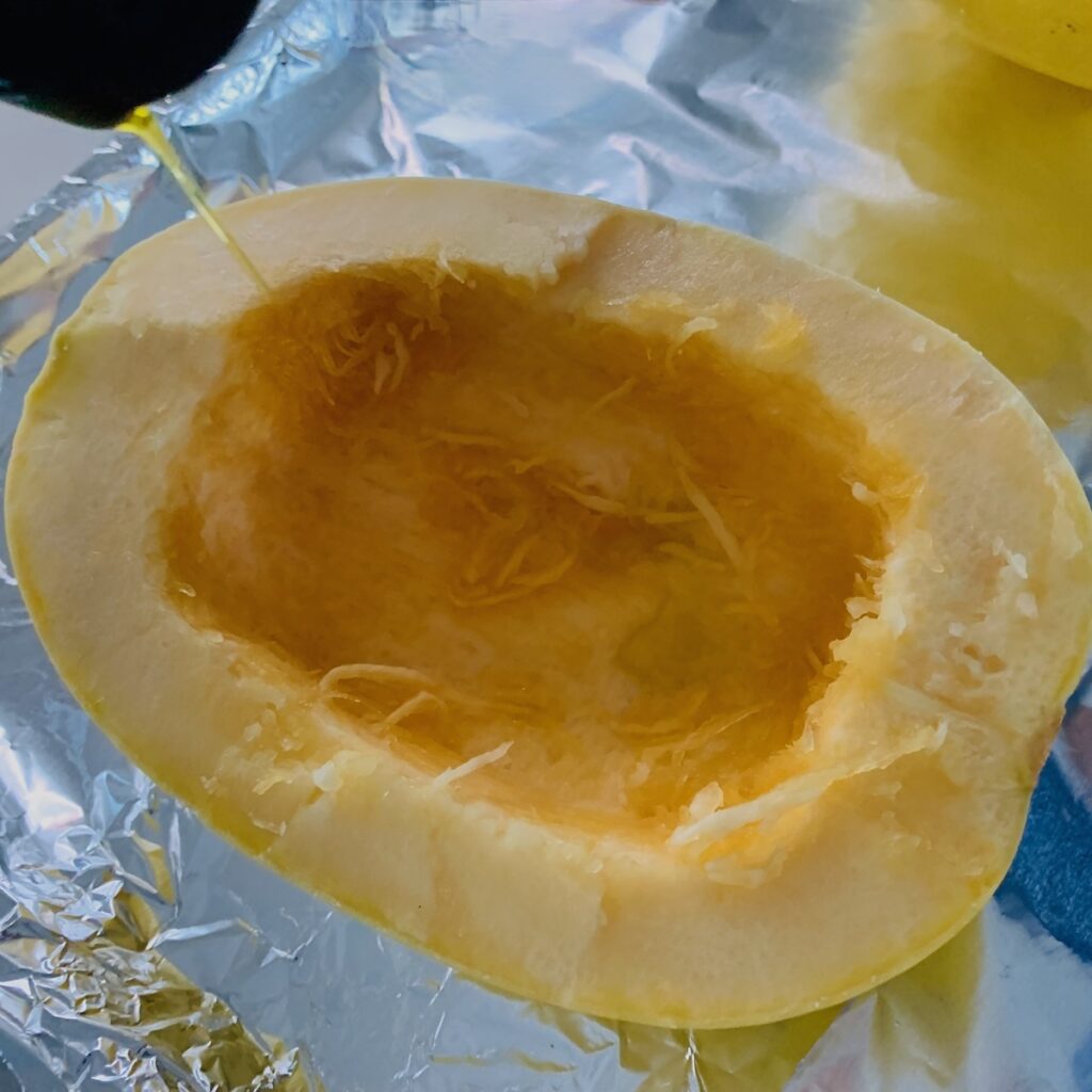 Raw spaghetti squash with seeds removed and a little olive oil being drizzled on top.