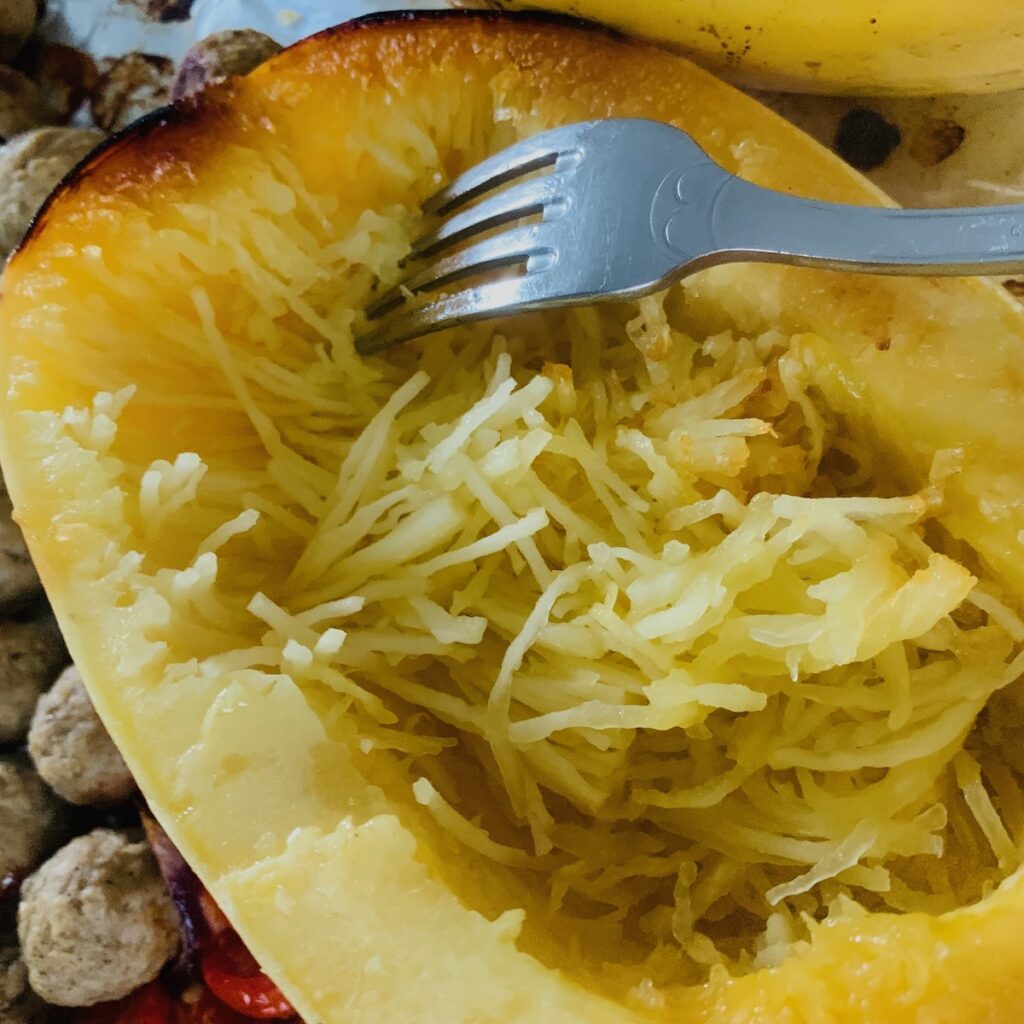 A fork shredding the inside of the spaghetti squash forming strands that look like spaghetti noodles.