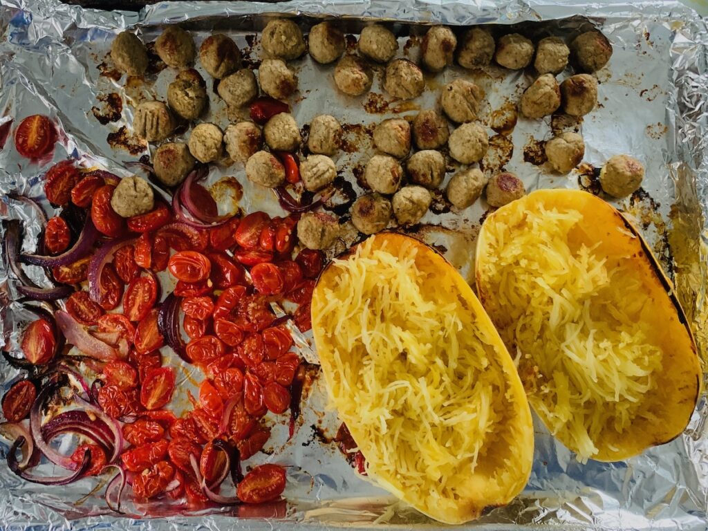 Birds Eye view: roasted tomatoes, onions, gluten-free meatballs and shredded spaghetti squash on a sheet pan.