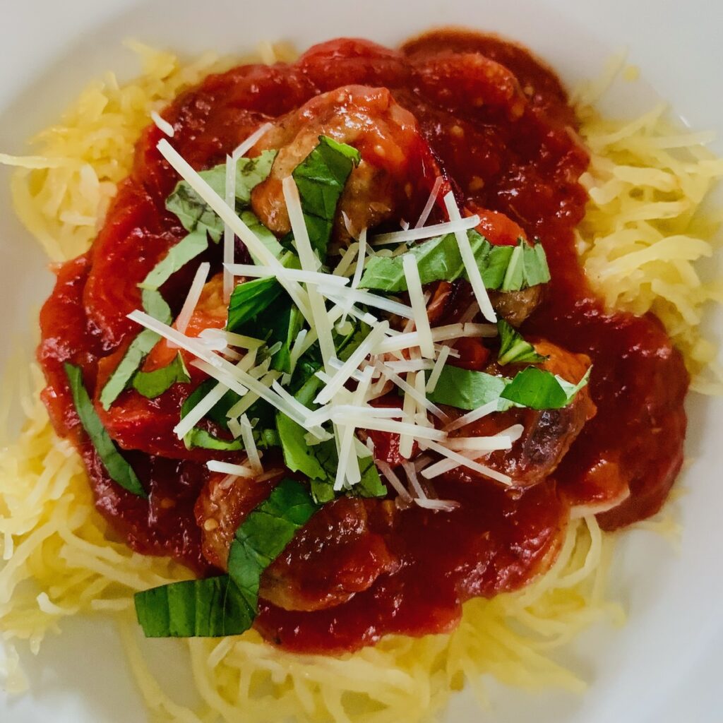Birds Eye view: round bowl with spaghetti squash topped with tomato sauce, meatballs, basil and shredded parmesan.