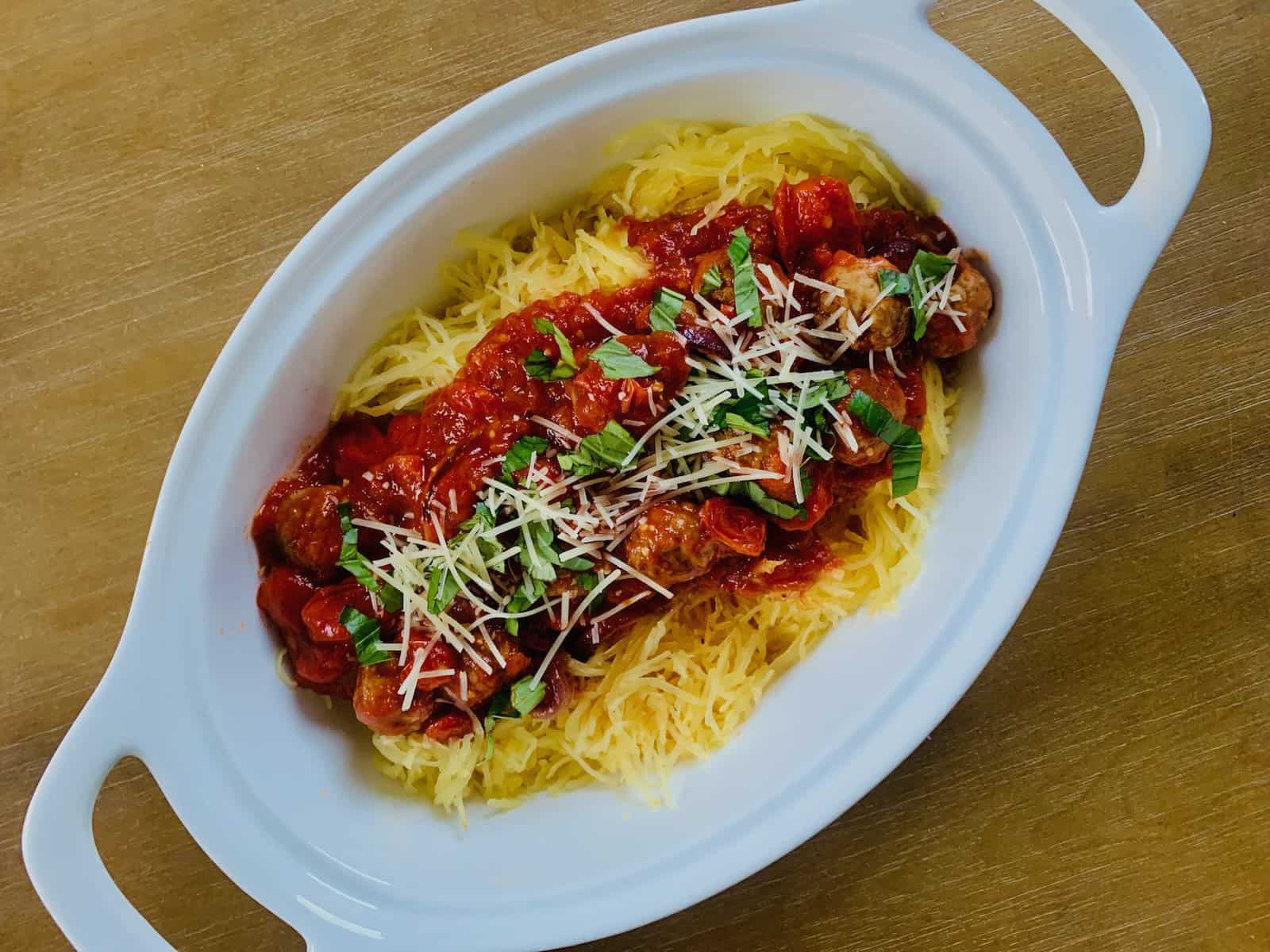 Birds Eye view: oval bowl with spaghetti squash topped with tomato sauce, meatballs, basil and shredded parmesan.