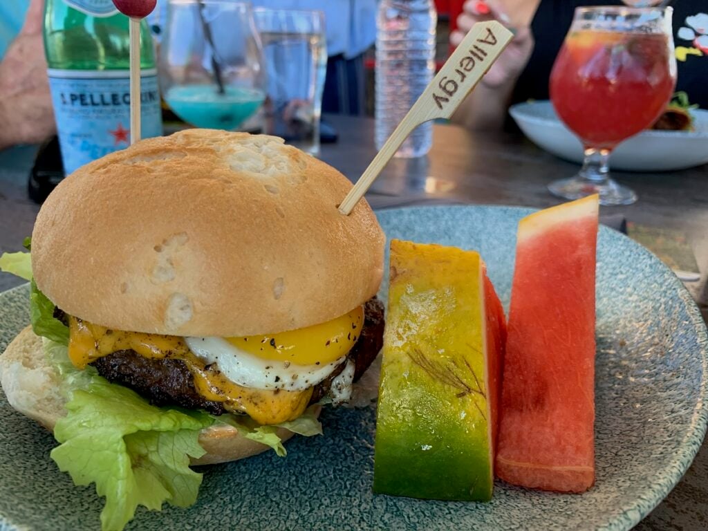 Burger with egg and an allergy pick and two slices of watermelon.