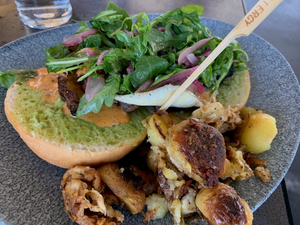 Open faced burger buns topped with steak and greens with an allergy pick, and a side of roasted potatoes.