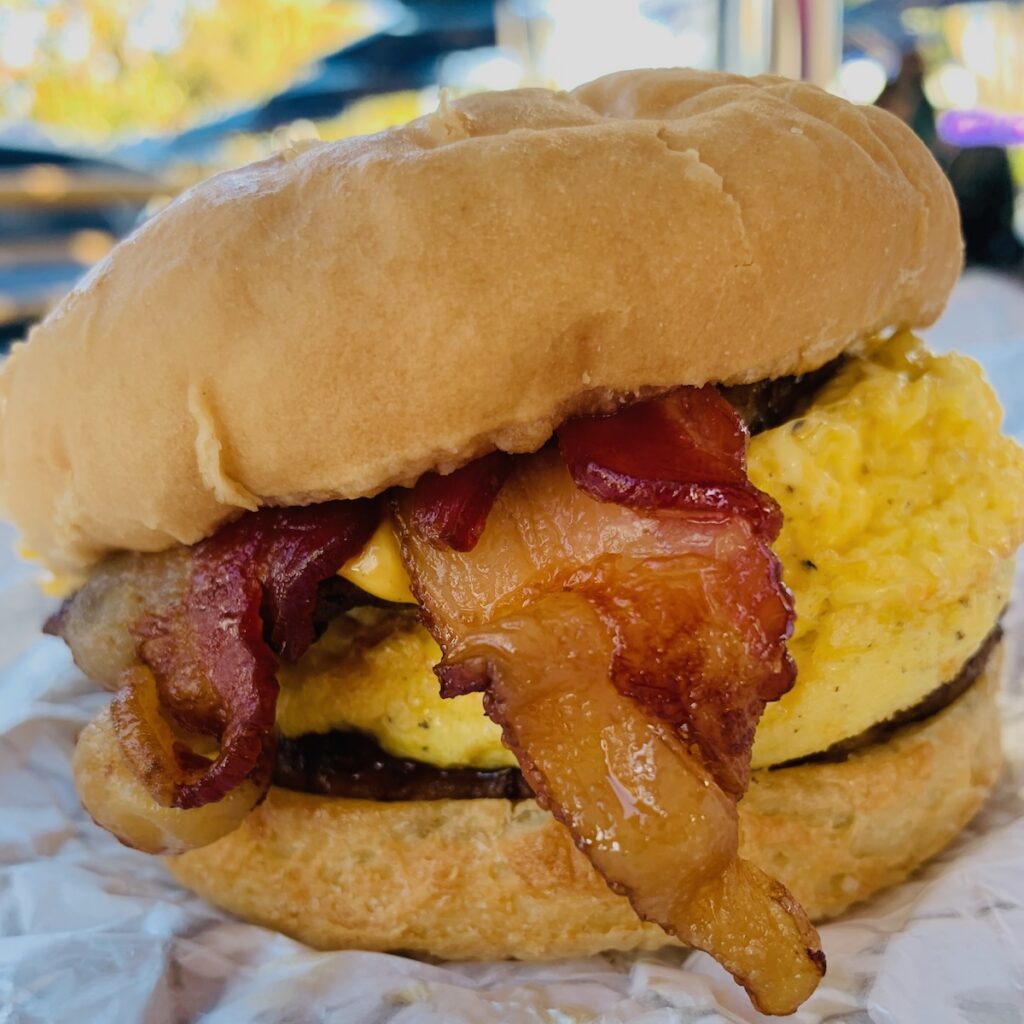 Breakfast sandwich on a gluten-free bun with visible eggs and bacon.