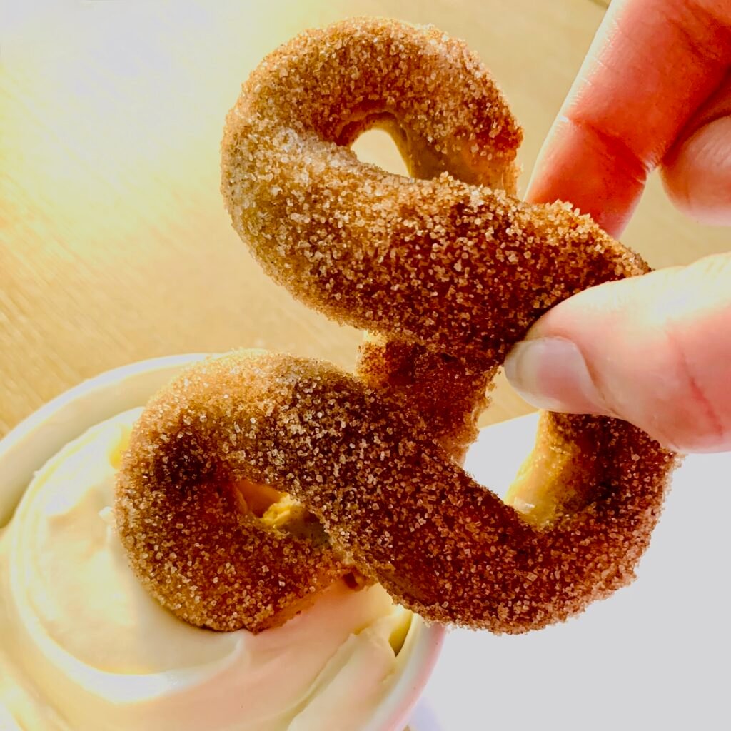 Mickey churro pretzel being dipped in cream cheese frosting dip