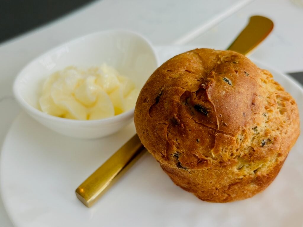 rosemary roll with gold knife and tiny bowl of butter on a plate
