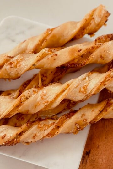 Baked parmesan cheese straws on a wood and marble cutting board.