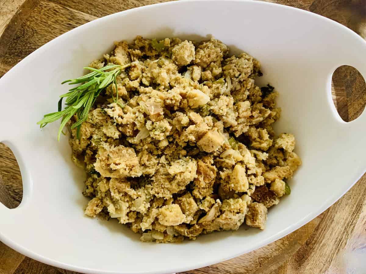 Stuffing in a white oval bowl with a sprig of rosemary.